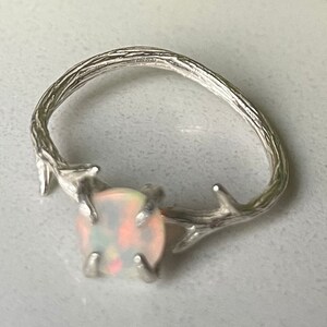 May include: A silver ring with a delicate branch design and a white opal gemstone.