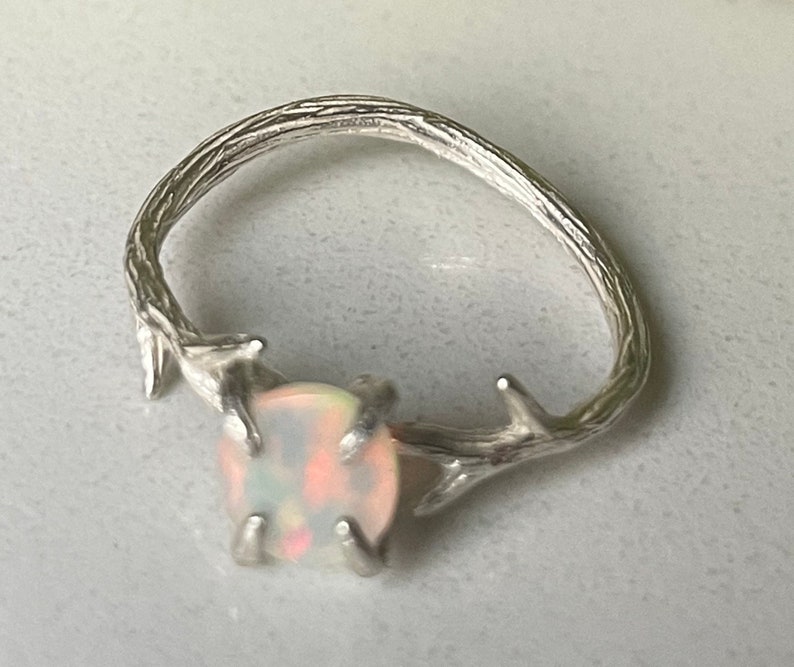 May include: A silver ring with a delicate branch design and a white opal gemstone.