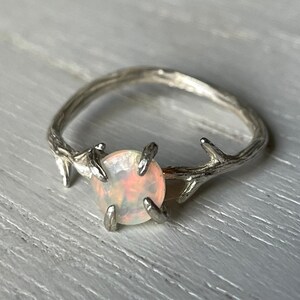 May include: A silver ring with a delicate twig design and a round, white opal gemstone.