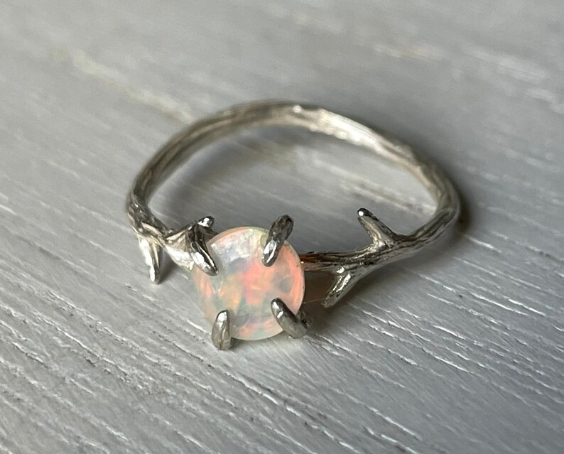 May include: A silver ring with a delicate twig design and a round, white opal gemstone.