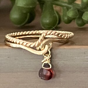 May include: A gold ring with a twisted rope design and a dangling garnet gemstone.