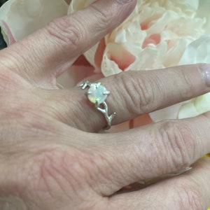 May include: A silver ring with a delicate branch design and a white opal gemstone.