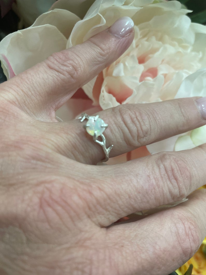 May include: A silver ring with a delicate branch design and a white opal gemstone.