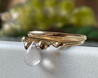 May include: A gold ring with a delicate chain and a teardrop-shaped pink crystal pendant.
