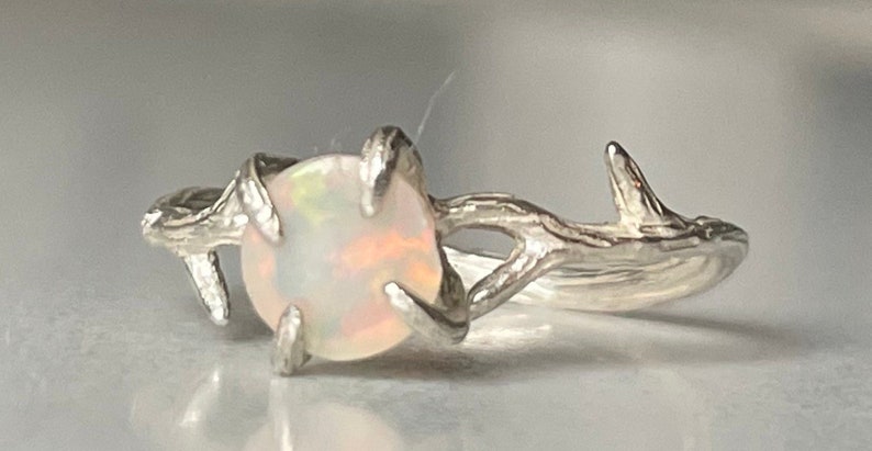 May include: A silver ring with a white opal gemstone set in a branch-like design.