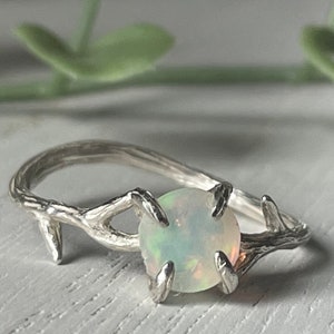 May include: A silver ring with a delicate branch design and a white opal gemstone.