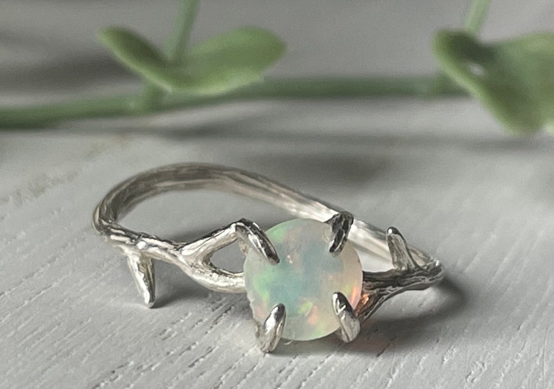 May include: A silver ring with a delicate branch design and a white opal gemstone.