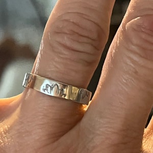 May include: A silver band ring with an inscription on the outside of the band.