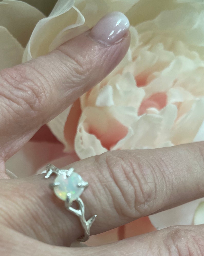 May include: A silver ring with a white opal gemstone set in a branch design.