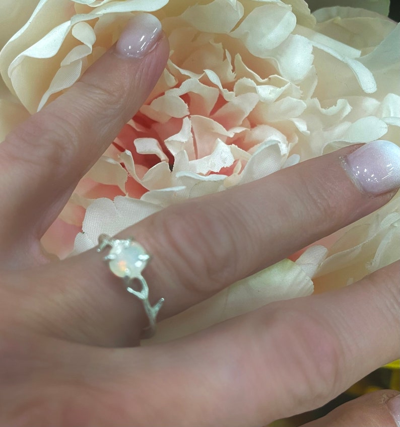 May include: A silver ring with a white opal stone set in a branch design.