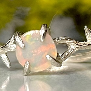 May include: A silver ring with a white opal gemstone set in a branch-like design.