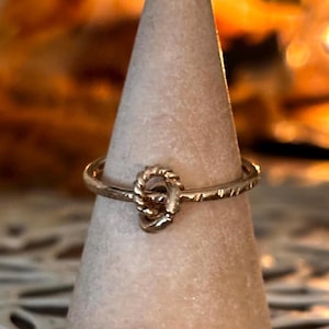 May include: A gold ring with a knot design. The ring is on a display stand.