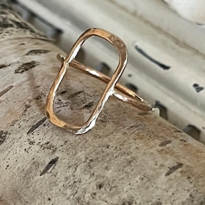 May include: A gold-toned ring with a hammered, rectangular design. The ring is open on one side and has a smooth, rounded band.