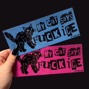 May include: Two rectangular stickers, one blue and one pink, with black text and a black cat illustration. The text on each sticker reads "My Cat says FUCK ice". The stickers are held against a black background.
