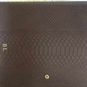 May include: A brown, faux snakeskin clutch with a gold snap closure. The initials "BL" are embossed in gold on the front. The clutch is rectangular and has a flap closure.