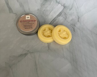 May include: Two round, yellow lotion bars with a bee design on top. The bars are in a tin with the text "T&C's Moisturizing Lotion Bar" on the label.
