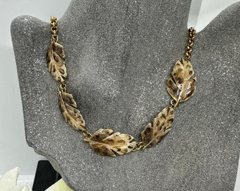 May include: A gold chain necklace with five brown and gold leaf-shaped pendants. The leaves have a textured, speckled pattern.