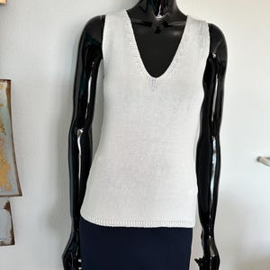 May include: A white sleeveless knitted top with a v-neckline. The top is made of a soft, lightweight fabric and has a relaxed fit.