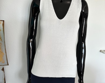 May include: A white sleeveless knitted top with a v-neckline. The top is made of a soft, lightweight fabric and has a relaxed fit.