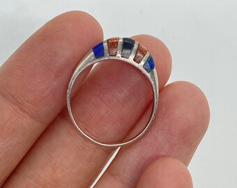 Puede incluir: Un anillo de plata con una banda de piedras incrustadas. Las piedras son azules, negras y naranjas.