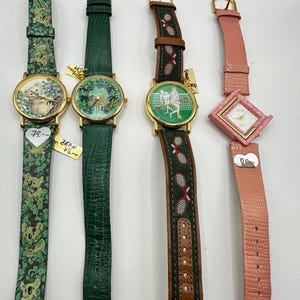 Puede incluir: Cuatro relojes de pulsera con diferentes correas de cuero de colores y diseños de esfera. Los relojes presentan un koala, una escena de la jungla, un jugador de tenis y una esfera cuadrada con fondo blanco.