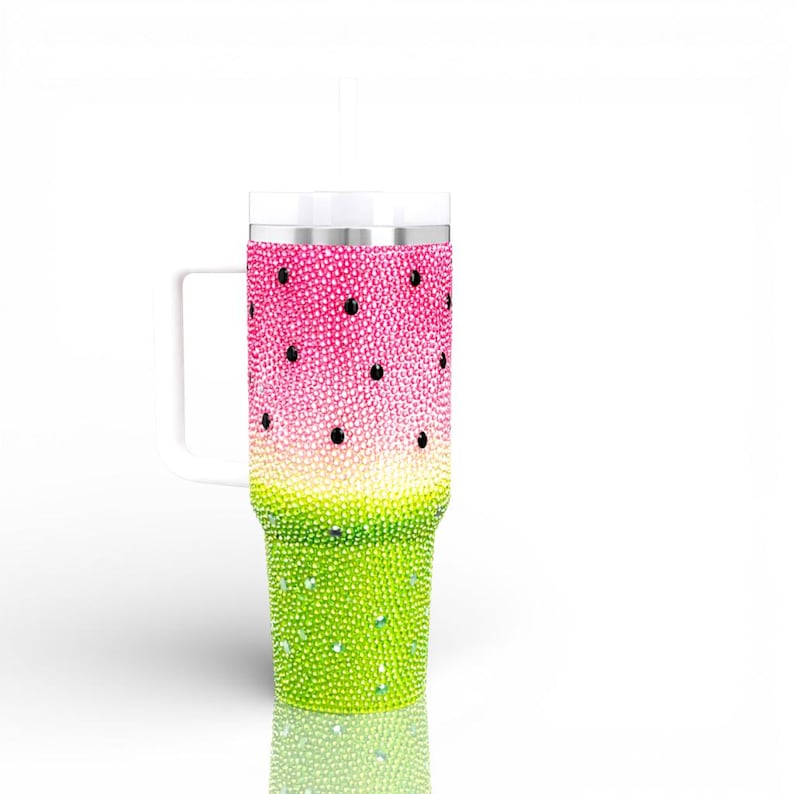 Puede incluir: Un vaso alto y aislado con un asa blanca, decorado para parecerse a una sand&iacute;a. La mitad superior es rosa con acentos negros en forma de semillas, que transicionan a verde en la parte inferior. Toda la superficie est&aacute; cubierta de brillantes pedrer&iacute;a.