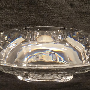May include: A clear glass candle holder with a textured design. The holder has a wide, shallow bowl and a raised center for a candle.