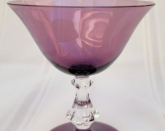 May include: A purple glass goblet with a clear glass stem and base. The goblet has a wide, shallow bowl and a delicate, ornate stem.