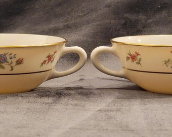 May include: Two white porcelain teacups with a floral pattern and gold trim. The cups have two handles and are perfect for serving tea or coffee.