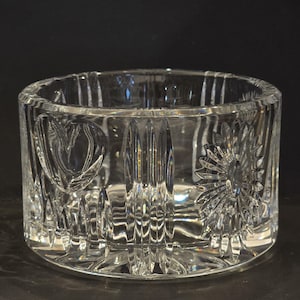 May include: A clear, cylindrical glass bowl featuring a series of vertical fluted panels around the exterior. The glass surface is decorated with alternating embossed motifs, including a heart shape and a multi-petaled flower design.