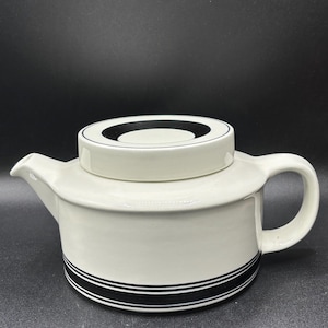 May include: White ceramic teapot with a black and white striped design around the bottom. The lid has a black circle design.