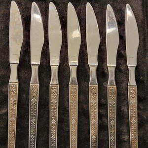 May include: Set of eight silver dinner knives with ornate floral designs on the handles.
