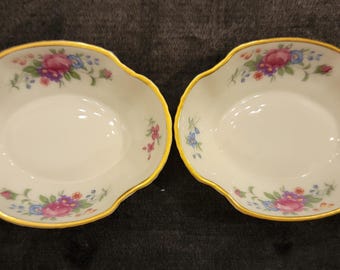 May include: Two white, scalloped-edge dishes with a gold rim and floral pattern. The floral design includes pink, blue, and purple flowers with green leaves. The dishes are likely for serving small portions.