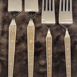 May include: Four silver forks with ornate floral designs on the handles. The forks are arranged in a row from largest to smallest.