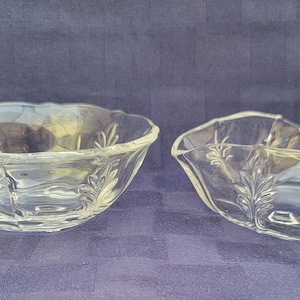 May include: Two clear glass bowls with a scalloped edge and a floral design. One bowl has a handle.