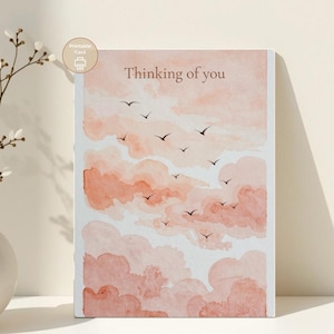Puede incluir: Tarjeta de felicitación rectangular con el texto "Thinking of you" sobre un fondo de acuarela de nubes color melocotón y pájaros volando. La tarjeta tiene un borde blanco. Un pequeño icono que dice "Printable Card" está en la esquina superior izquierda.