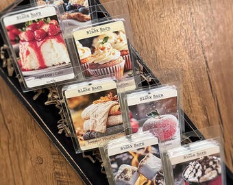May include: A selection of The Black Barn scented wax melts in clear plastic packaging. The scents include Angel Food Cake, Muffins, Sweater Weather, Apple, Campfire Marshmallow, and Chocolate. Each melt is 3 oz/85g.