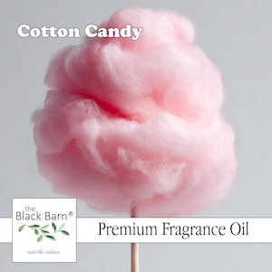 May include: A fluffy, light pink cotton candy on a wooden stick. The text "Cotton Candy" is above the cotton candy, and the text "Premium Fragrance Oil" is below it. The Black Barn logo is in the lower left corner.