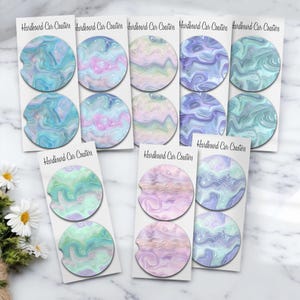 May include: A collection of hardboard car coasters with a marbled design. The coasters feature swirls of blue, pink, purple, and green. Each coaster set is displayed on a white card with the text "Hardboard Car Coasters".