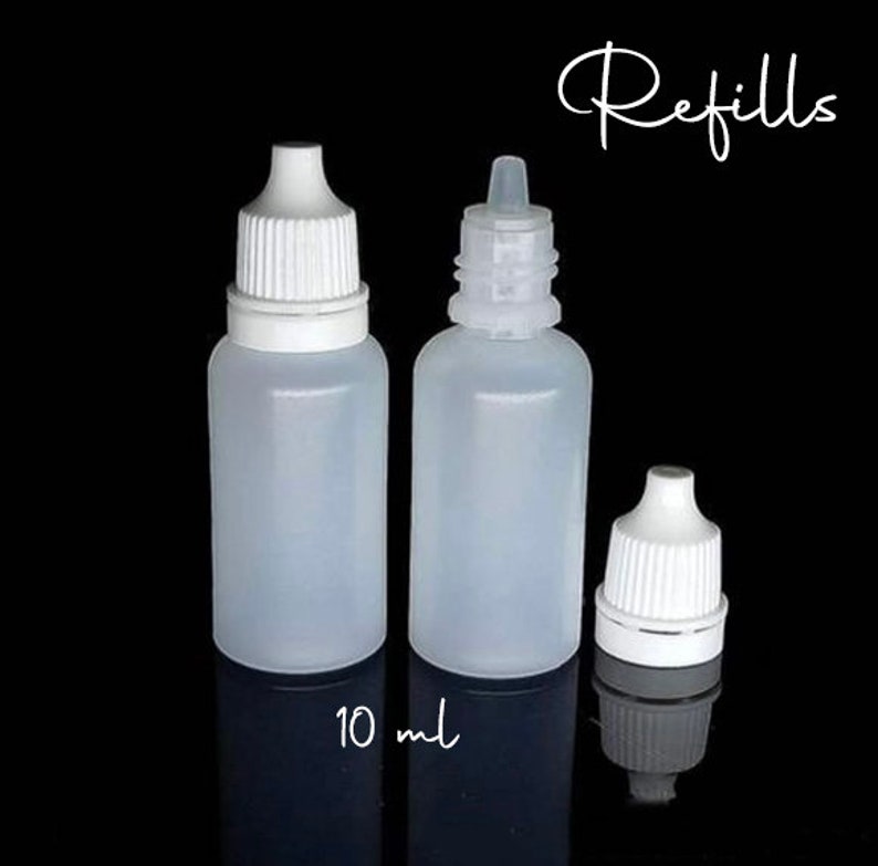 May include: Three clear plastic dropper bottles with white caps and the word "Refills" in cursive. The bottles are labeled "10 ml". The bottles are on a black background.