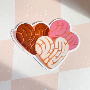 May include: Three heart-shaped pan dulce pastries, one brown, one white, and one pink, with a swirl design.