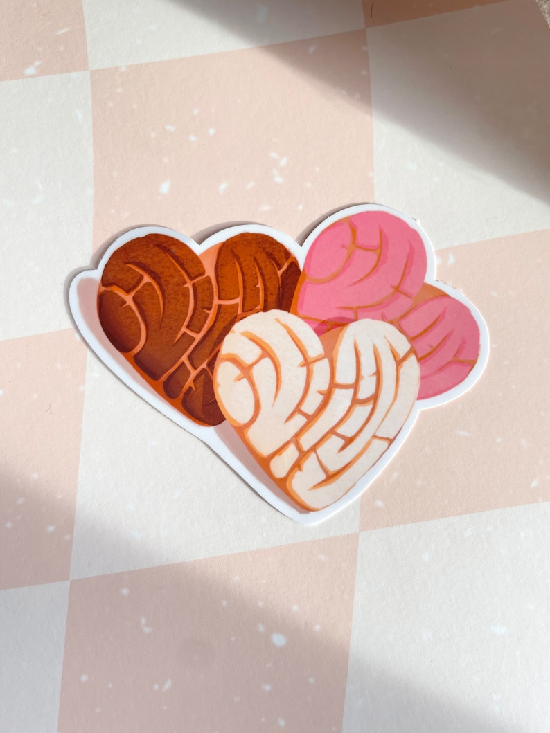May include: Three heart-shaped pan dulce pastries, one brown, one white, and one pink, with a swirl design.