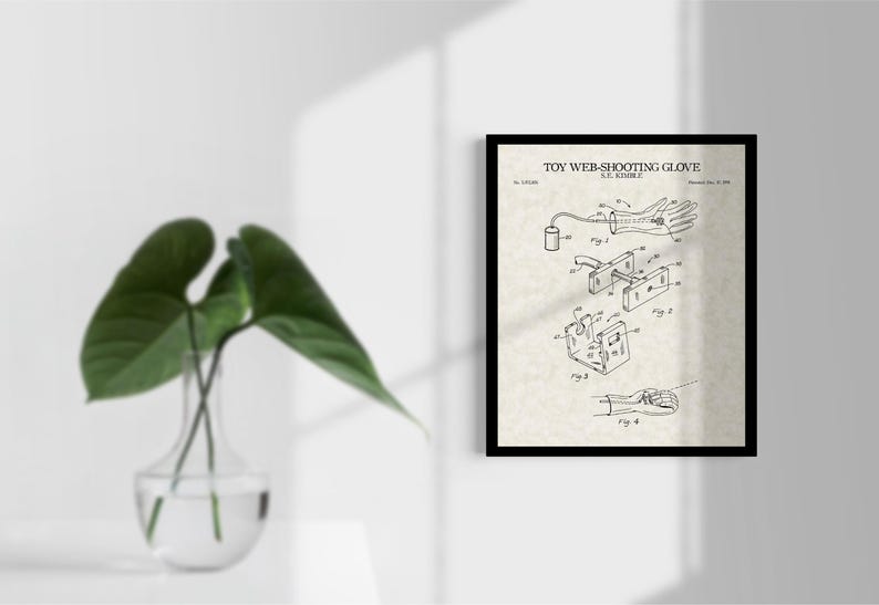 Peut inclure: Impression encadr&eacute;e d'un brevet de &laquo; Toy Web-Shooting Glove &raquo; avec des sch&eacute;mas d&eacute;taill&eacute;s. L'impression est sur un fond cr&egrave;me. Un vase en verre transparent avec des feuilles vertes est au premier plan.