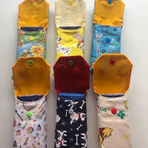 May include: Six rectangular fabric pouches with snap closures, each featuring distinct patterns including bees, dalmatians, tools, art supplies, dogs with bones, and cartoon bears. The pouches are lined with solid yellow or red fabric.