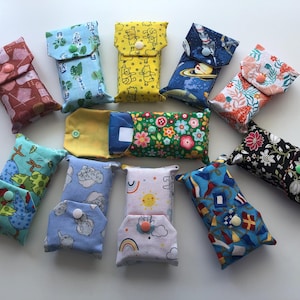 May include: A collection of eleven rectangular fabric pouches with snap closures, featuring various colourful patterns including floral, space, animal, and geometric prints. Each small pouch is designed to hold items securely with a plastic snap button.