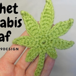 May include: A crocheted green cannabis leaf with a stem. The leaf is held in a hand. The text "Crochet Cannabis Leaf" and "BY: DREAM9DESIGN" is visible in the image.