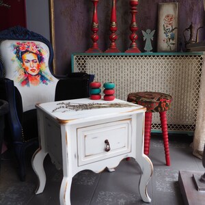 Può includere: Tavolino da divano in legno bianco con un cassetto e gambe ornate. Il tavolo ha una finitura invecchiata ed è decorato con lavanda secca. Il tavolo è su un pavimento di piastrelle grigie.