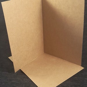 Op de afbeelding: Een blanco, bruine kaart gevouwen in de helft. De kaart is gemaakt van een getextureerd papier.