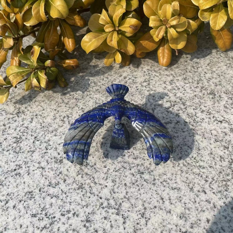 May include: A blue and grey lapis lazuli carving of a bird with outstretched wings. The bird is perched on a small base.