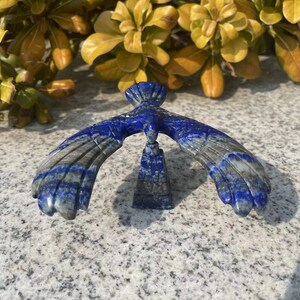 May include: A blue and grey lapis lazuli bird sculpture with outstretched wings, perched on a small, square base.